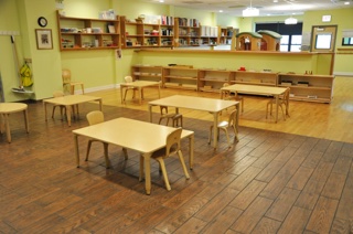 The toddler classroom, with child-height tables and chairs and open wooden shelves of materials